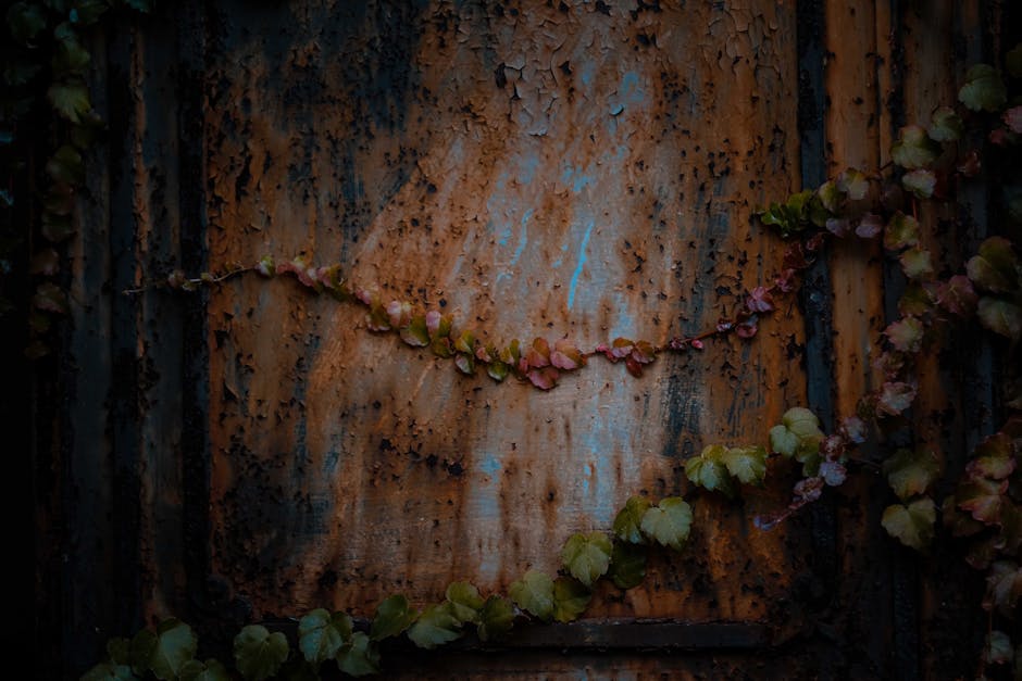 Aged damaged metal construction covered with corrosion and peeling paint placed on street near branches of plant with green leaves
