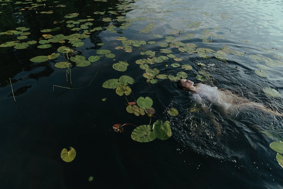 A woman peacefully floating in a lake surrounded by lily pads, creating a tranquil scene.