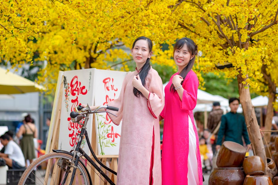 Women in traditional ao dai posing by a bicycle during Tet festival with yellow flowers.