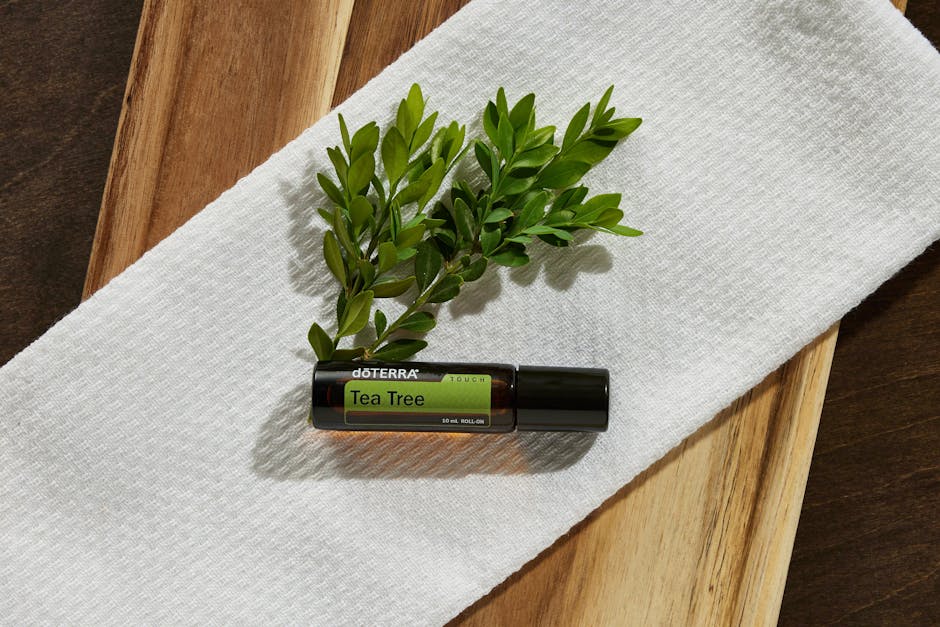 Tea tree oil bottle resting on white towel with green twig, highlighting natural beauty and wellness.