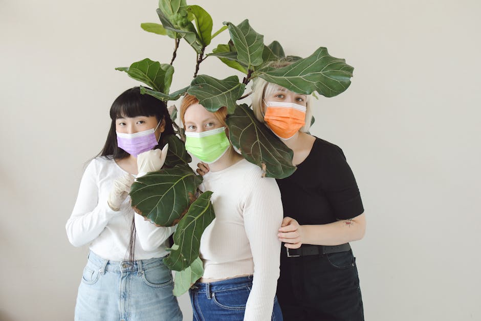 Three women in colorful masks stand behind a fiddle leaf fig, emphasizing pandemic safety and unity.