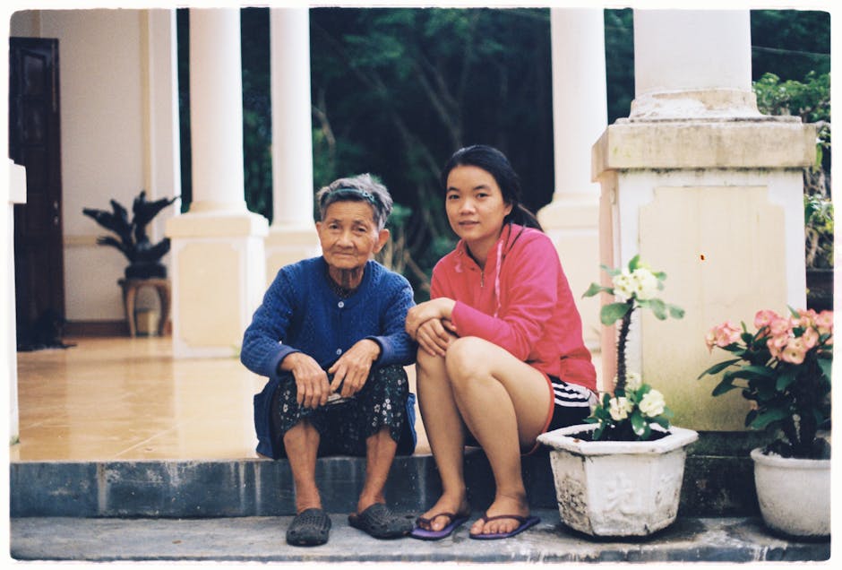 Elderly grandmother and granddaughter sitting together on a porch with potted plants.