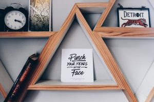 Triangular wooden bookshelf with motivational quote sign, clock, and decor.