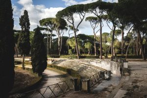 Serene view of an ancient Roman amphitheater surrounded by Italian pine trees in a tranquil park.