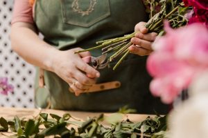 A florist delicately trims flower stems using pruning shears at a workspace.